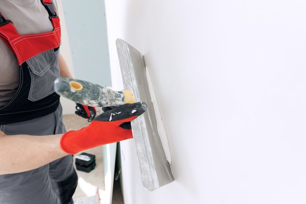 Een persoon gebruikt een pleistertroffel om egaliseermiddel gelijkmatig aan te brengen op een gestucte muur, als onderdeel van het proces van het glad maken van de muur.