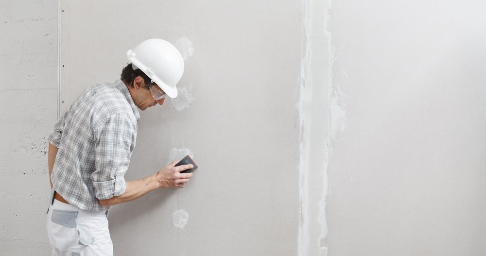 Een persoon gebruikt een spackmes om dunpleister gelijkmatig aan te brengen op een muur, als onderdeel van het proces van het aanbrengen van dunne laag stucwerk.