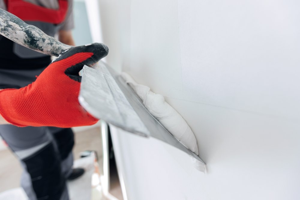 Een persoon gebruikt een pleistertroffel om muuregaliseermiddel gelijkmatig aan te brengen op een muur, als onderdeel van het proces van het glad maken van muren.
