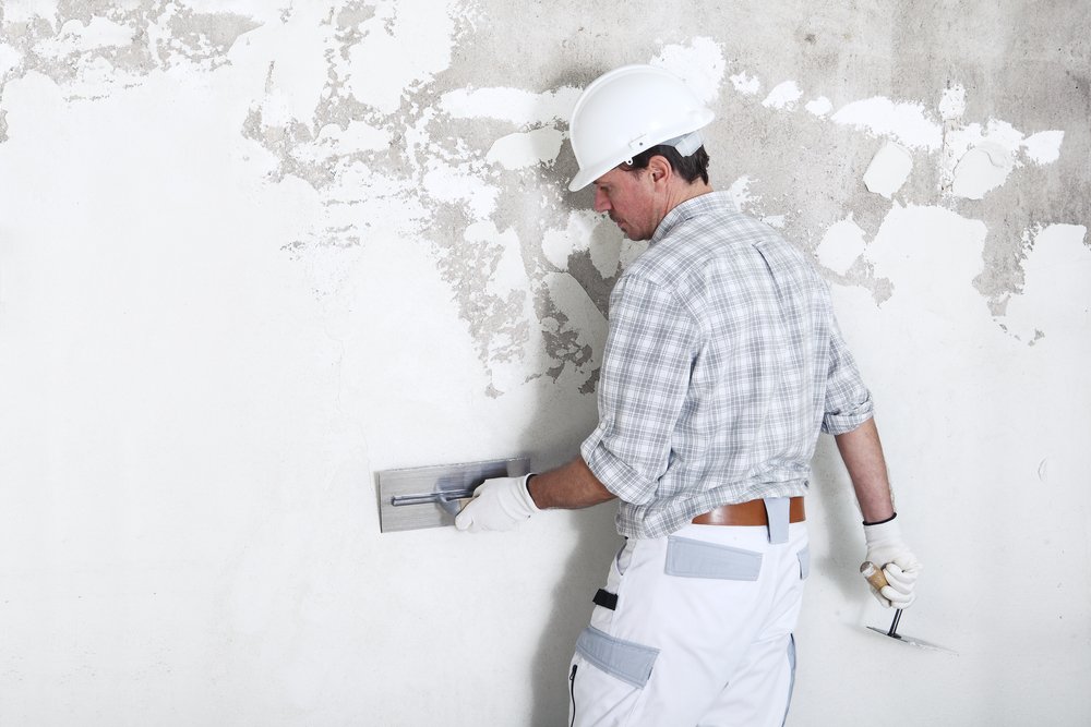 Een persoon gebruikt een pleistertroffel om muuregaliseermiddel gelijkmatig aan te brengen op een oneffen muur, als onderdeel van het proces van het glad maken van de muur.