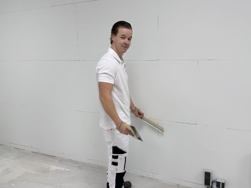 Vakman van Bouwsector Nederland staat lachend met een spaan in zijn hand voor een kale wand