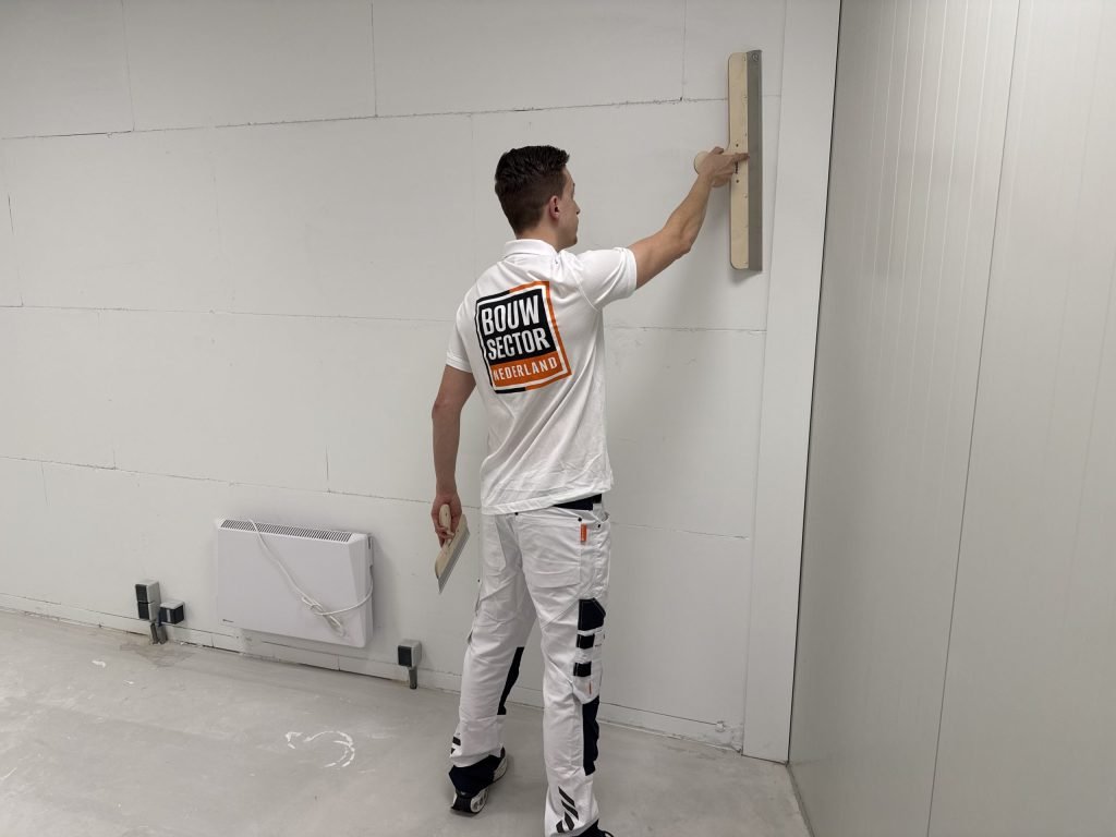 Vakman van Bouwsector Nederland trekt met een brede spaan een wand vlak in een lege ruimte met kale vloer