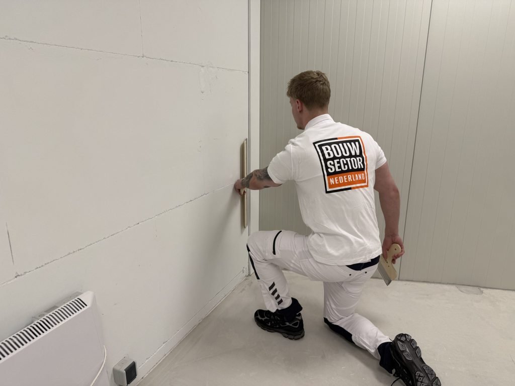 Vakman van Bouwsector Nederland werkt geknield met een spaan een naad in de hoek van een wand af